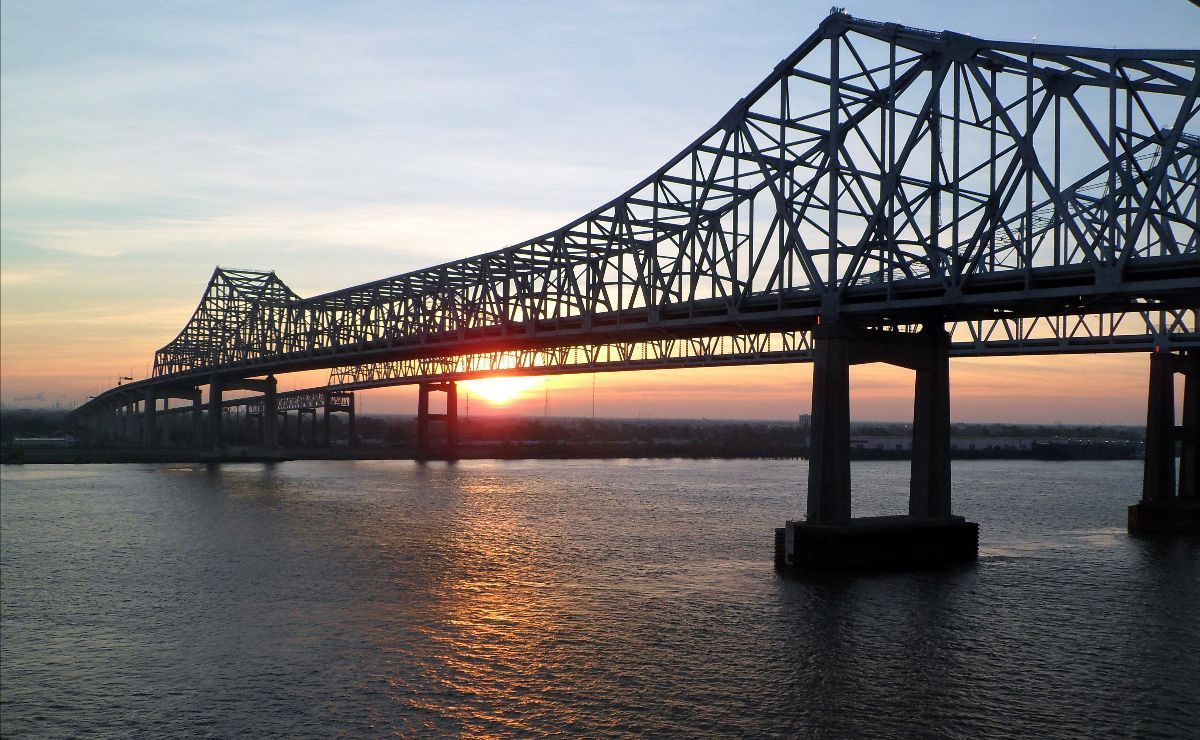 Bridge over water at sunset, with the sun's rays illuminating the horizon.
