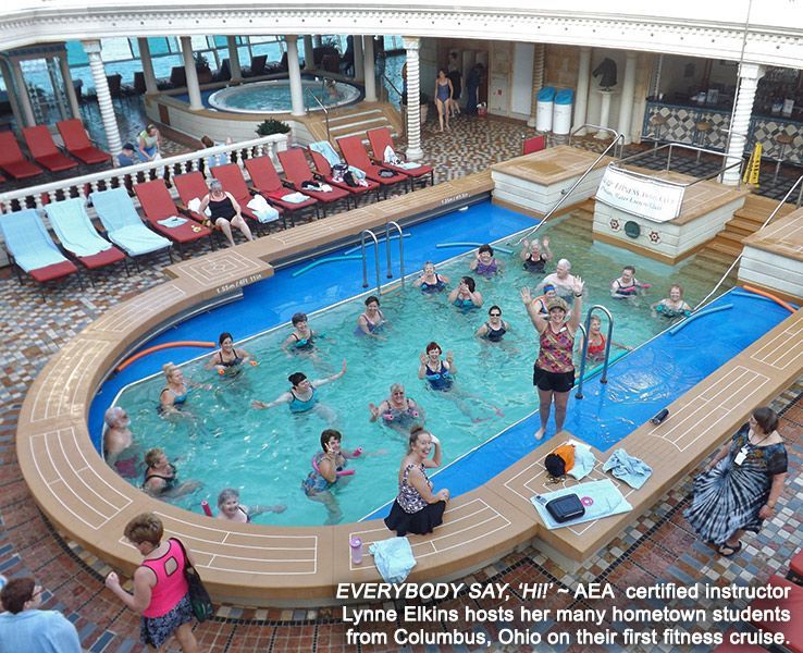 People doing water aerobics in a ship pool, led by an instructor, with lounge chairs nearby.