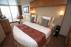 A cruise ship cabin featuring a bed, sofa, and balcony overlooking the sea.
