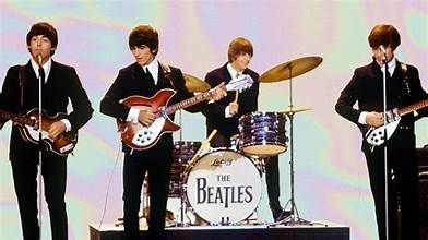 The Beatles, 1960s: John, Paul, Ringo, George, playing instruments on stage, wearing black suits.