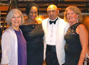 Four people dressed in formal attire smiling for the camera, indoors.