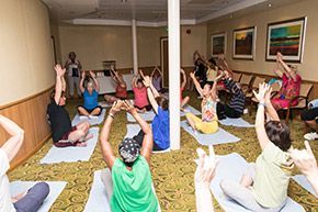 Group of people in yoga class, indoors, arms raised.