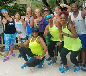 Group of smiling people in workout clothes posing outdoors.