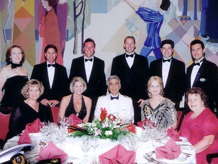 Formal dinner party with people in suits and gowns, seated at a decorated table.