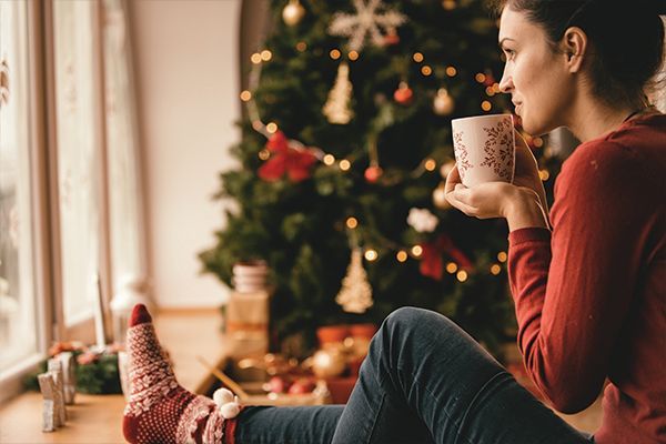 a woman is sitting on a window sill drinking a cup of coffee and looking out the window at a christmas tree .