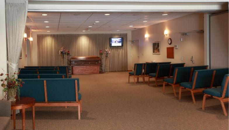 a funeral home with rows of green chairs and a television on the wall .