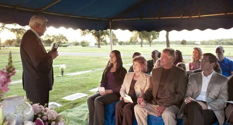 a man is giving a speech to a group of people sitting under a tent .