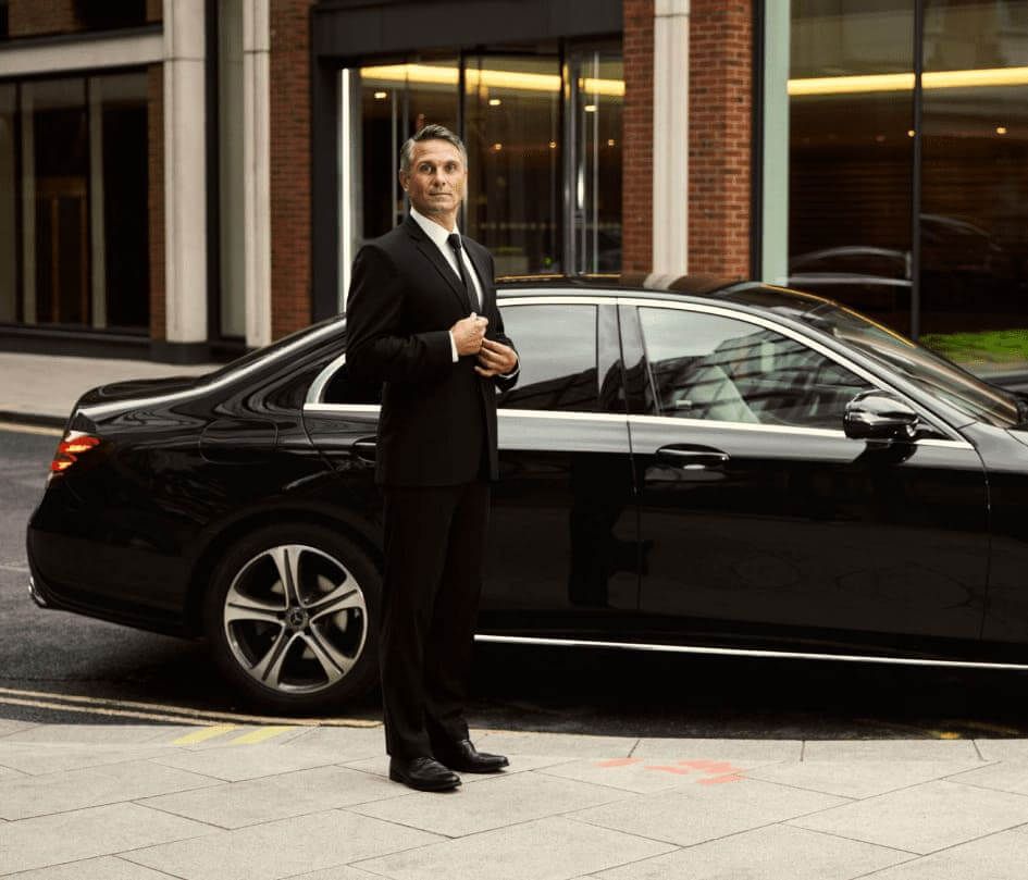A man in a suit and tie is standing next to a black car.