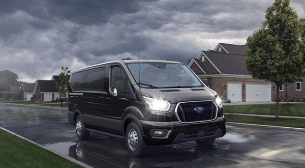 A black van is driving down a wet street in the rain.