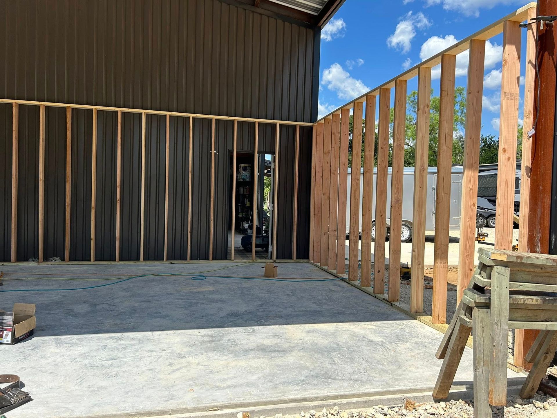Wooden wall framing being built against a dark building and concrete floor, with a partially open doorway.