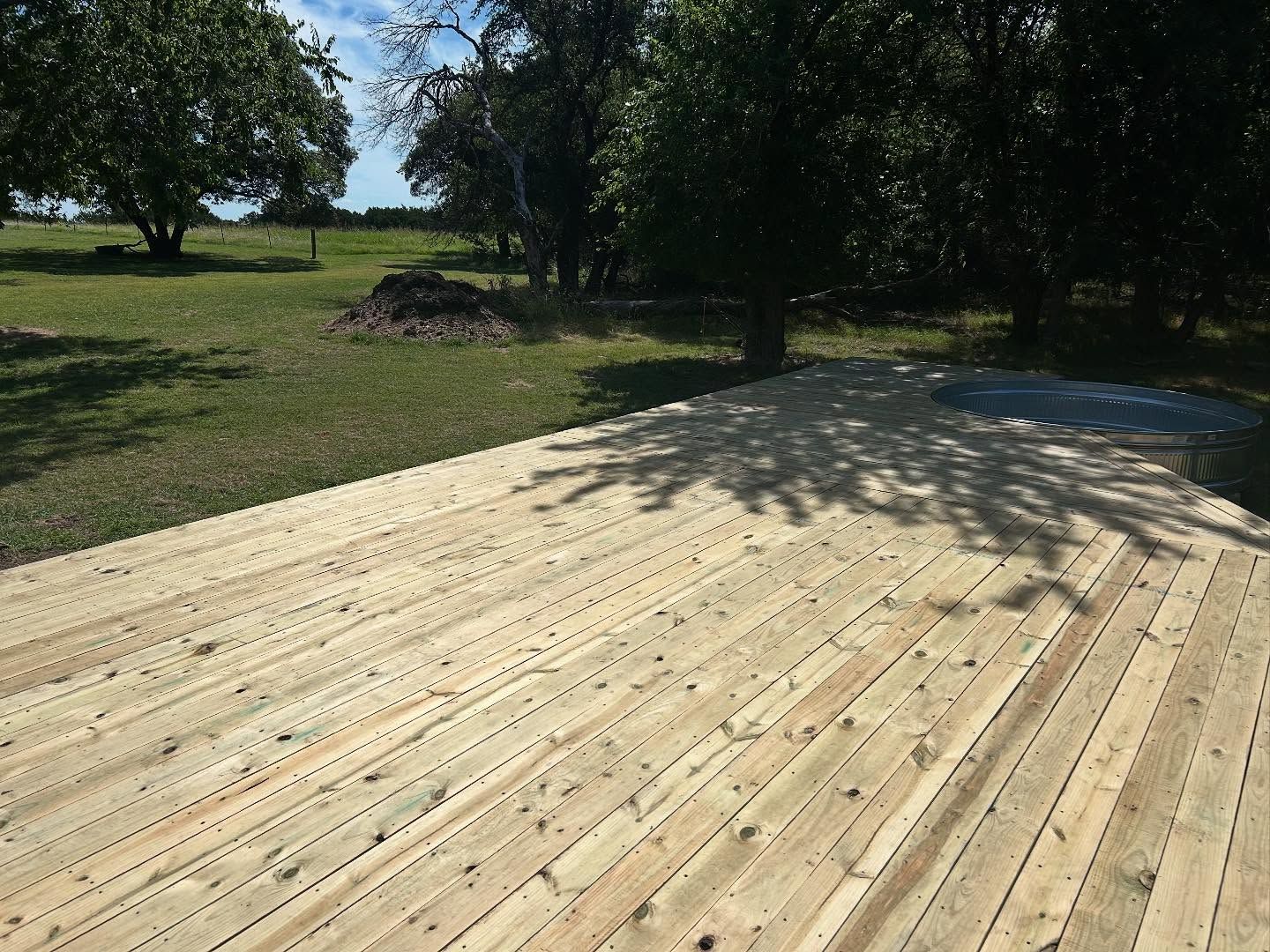 Wooden deck in a grassy yard, shaded by trees, on a sunny day.