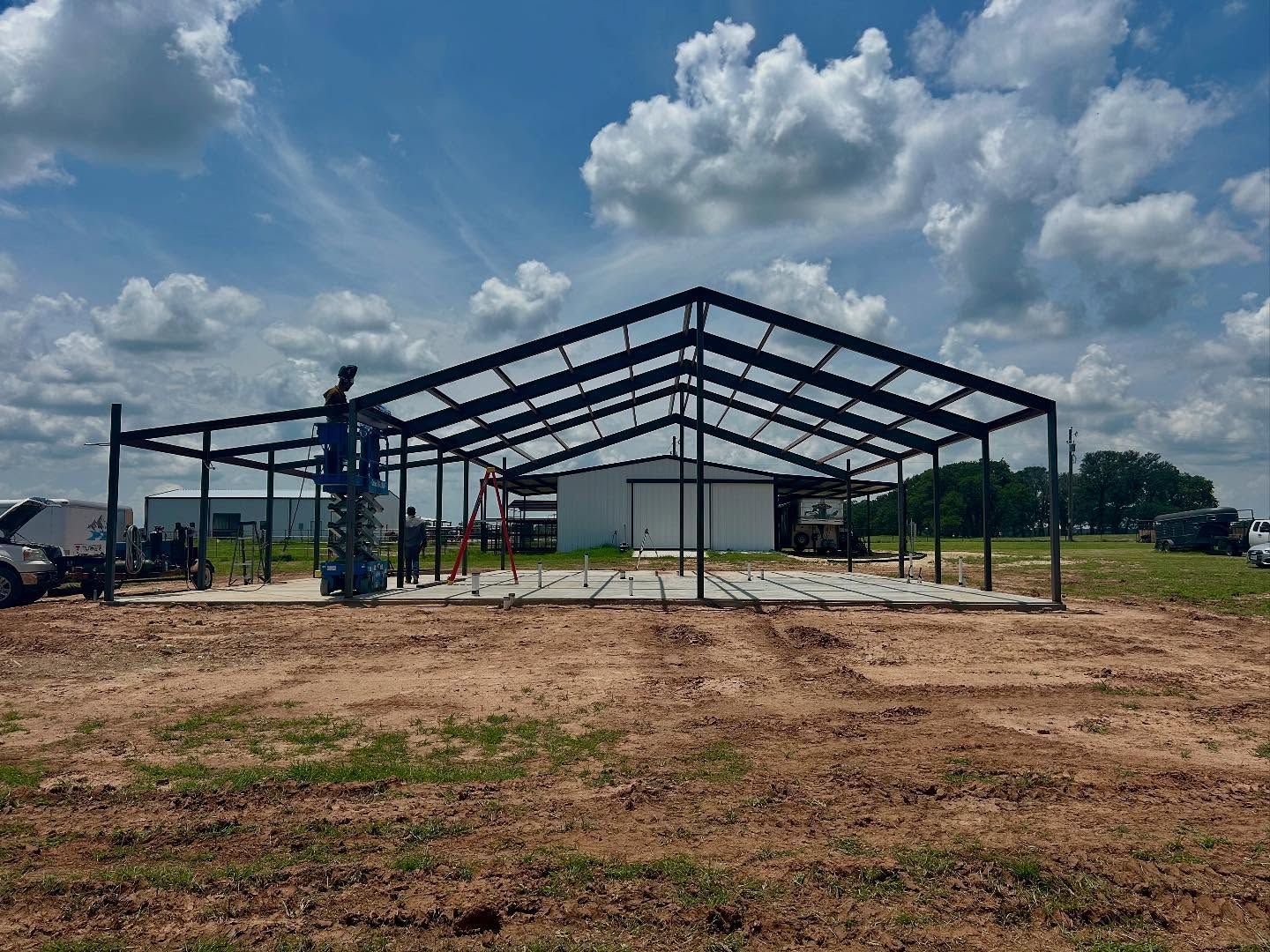 Steel frame building under construction on concrete foundation, blue sky with clouds.