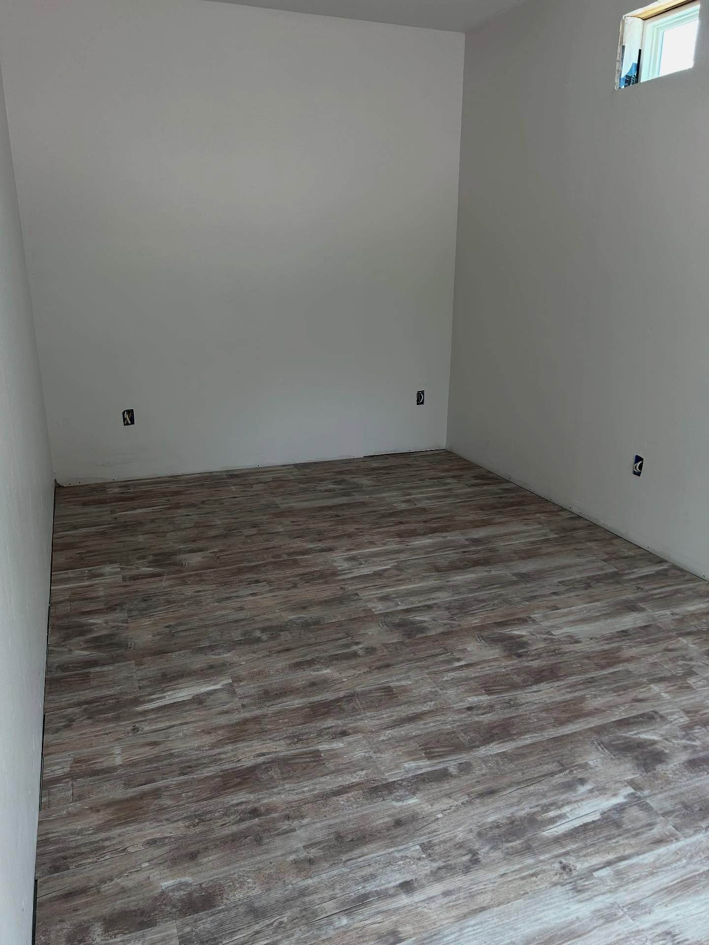 Empty room with wood-look flooring and white walls. Includes a small window and electrical outlets.