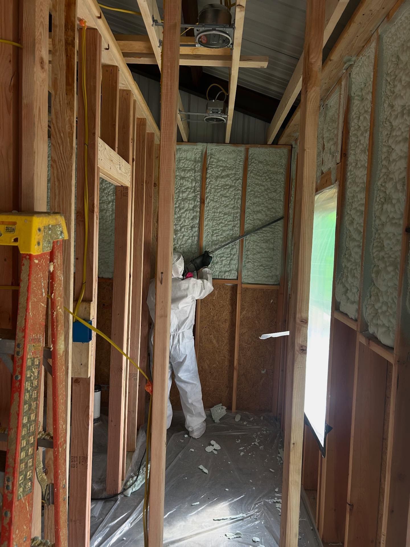Person in protective suit spraying insulation into a wall cavity in a building under construction.