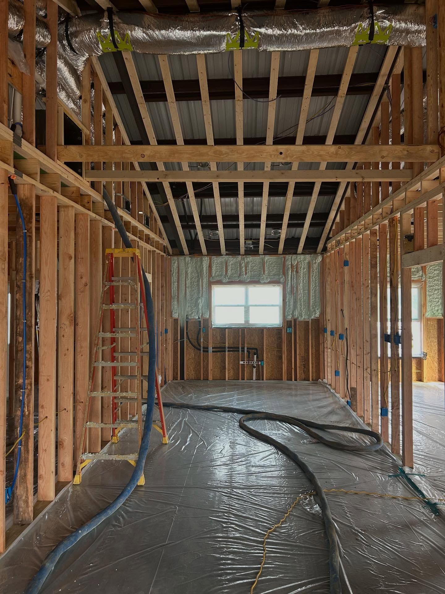 Interior view of a building under construction, showing exposed wooden framing, insulation, and a window.