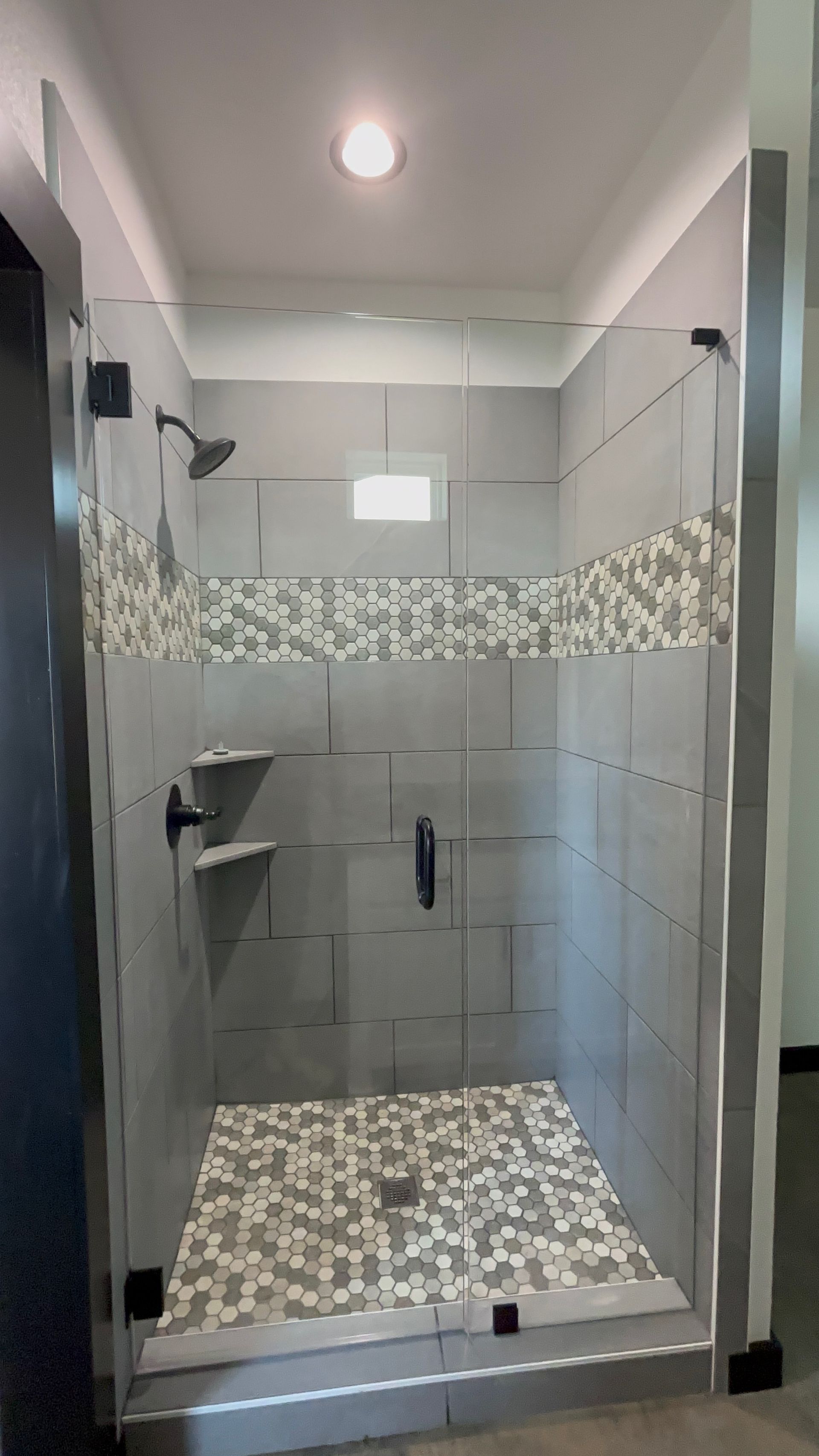Walk-in shower with gray tile, pebble floor, glass door, and mosaic tile accent.