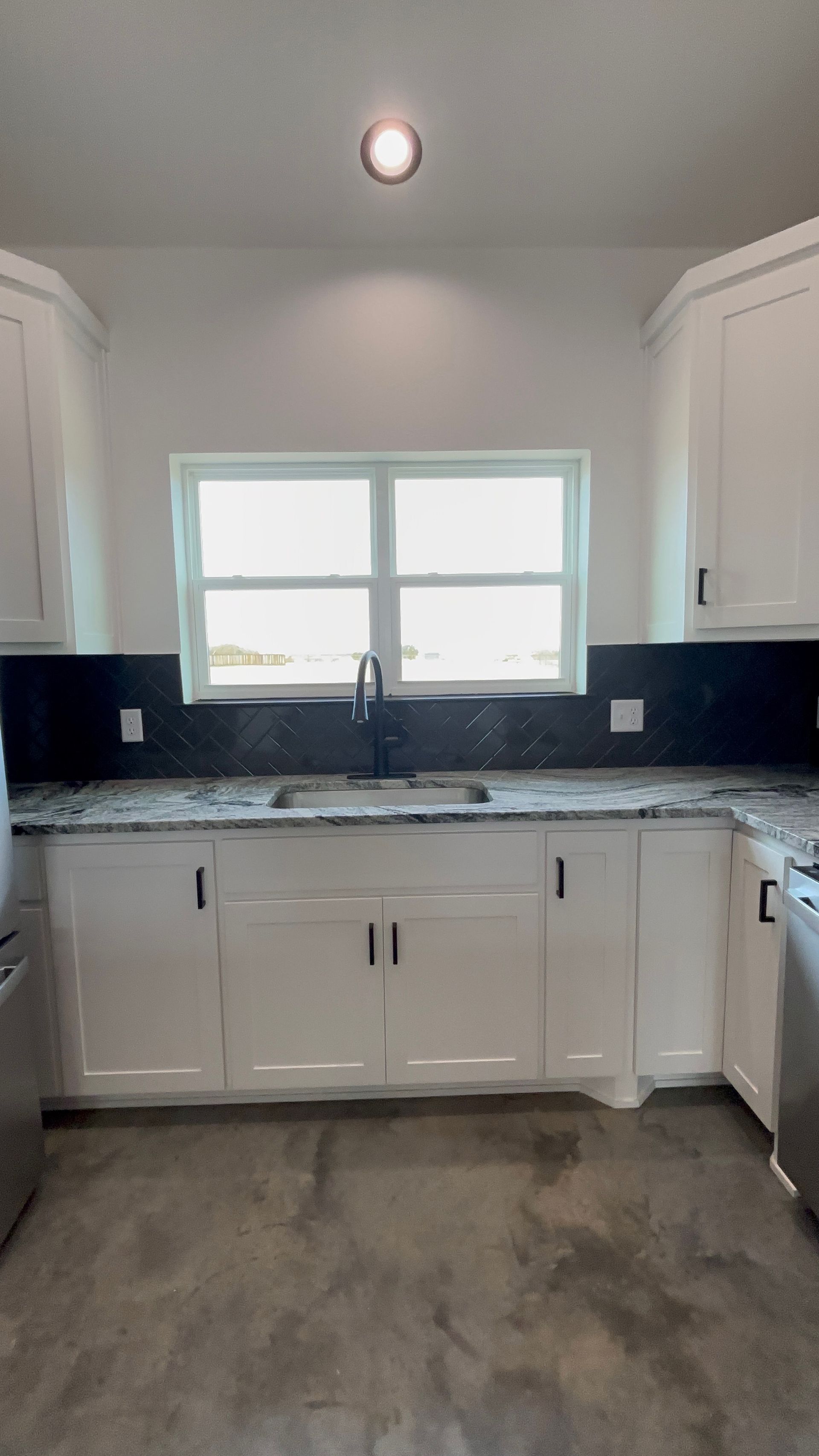 White kitchen cabinets with black countertops and a window.