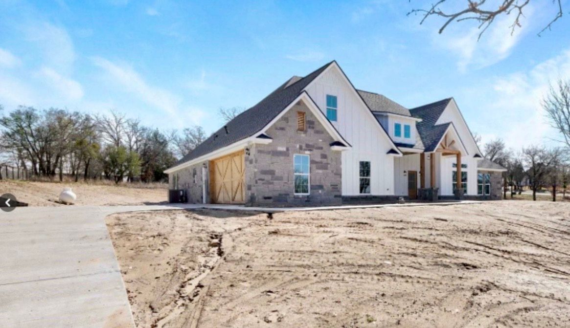 New construction house with stone and white siding, concrete driveway, and unfinished yard.