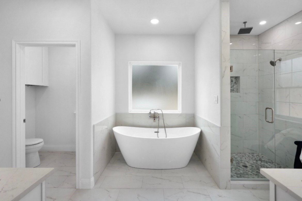 Modern white bathroom with a freestanding tub, shower, and toilet.