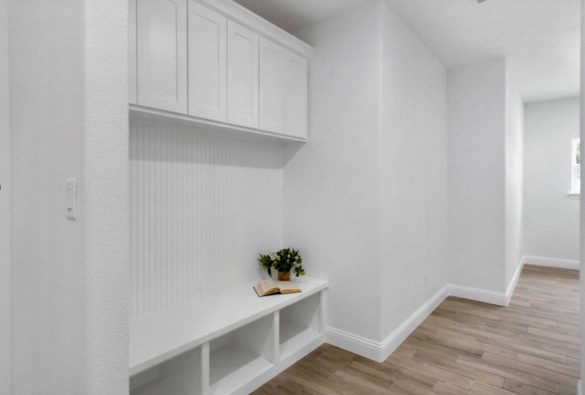 White mudroom with bench, storage, and cabinets. Light wood-look flooring.