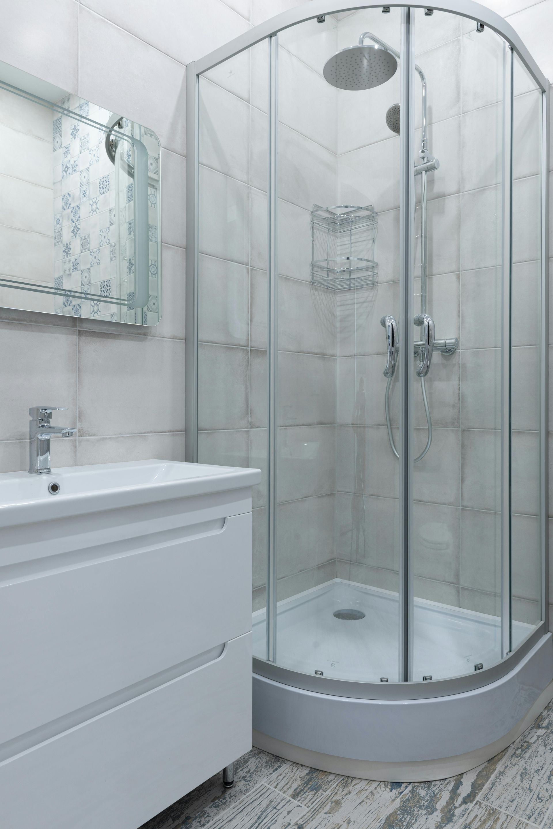 A modern bathroom with a white vanity, large curved glass shower, and tiled walls.