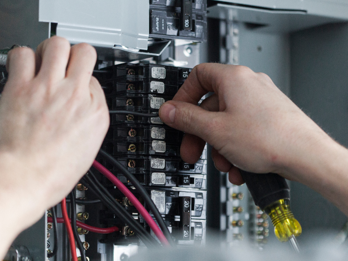 Hands working on an electrical panel, connecting wires.