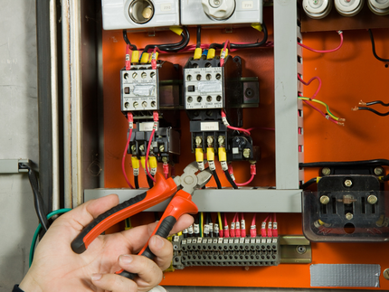 Hand using pliers on wires inside an electrical control panel with orange interior.