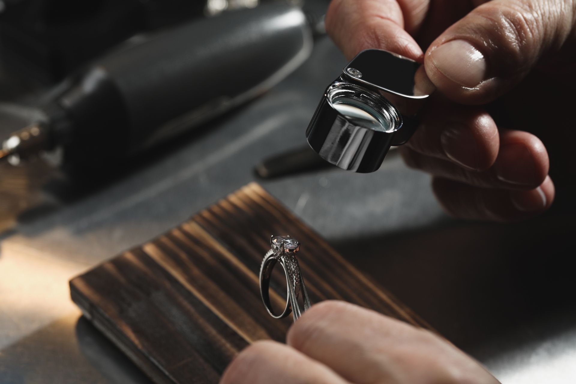 Appraiser examines diamond ring with loupe in workshop setting, checking quality and details.
