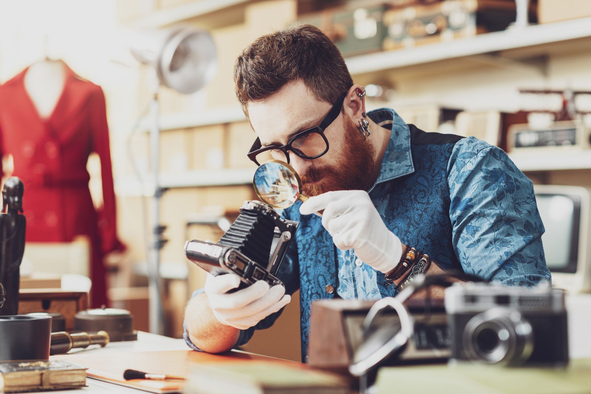 Person inspects vintage camera with magnifying glass in an appraisal shop setting.