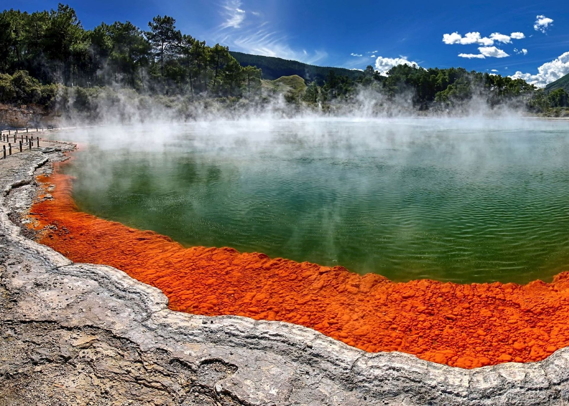 A wide-angle view of the Champagne Pool at Wai-O-Tapu, featuring vibrant orange mineral edges and steaming green water. Rotorua