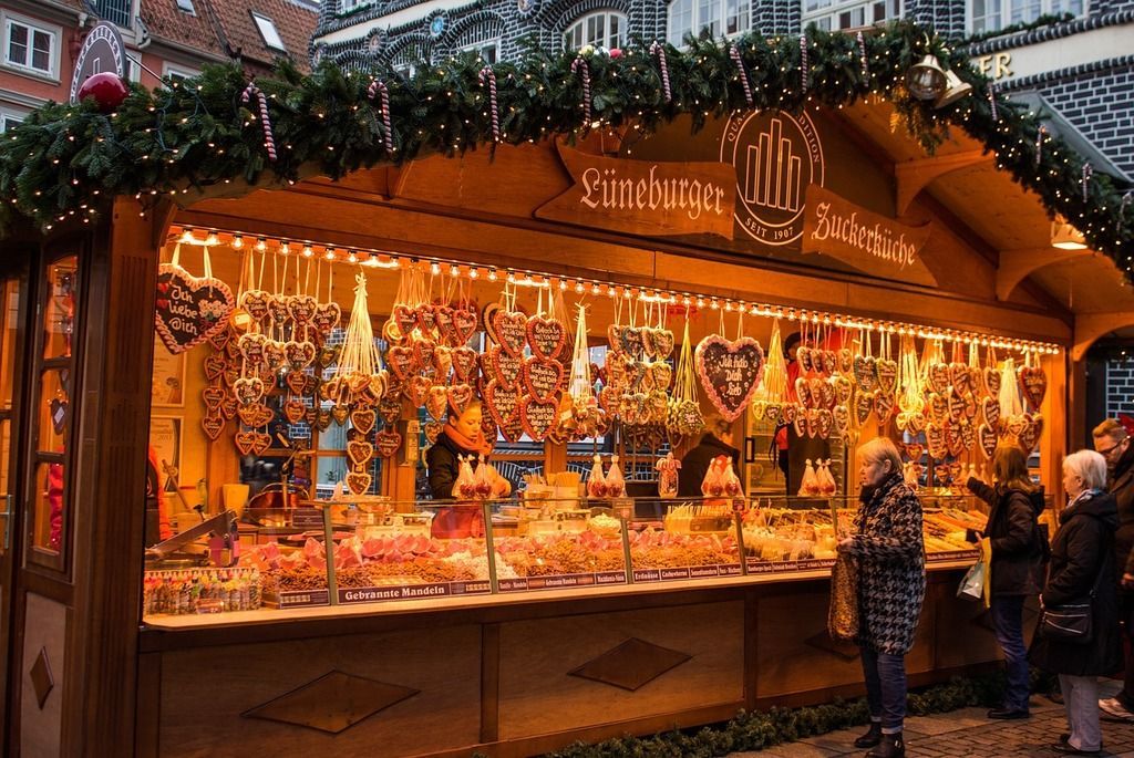 Christmas market stall, illuminated, selling sweets and ornaments. People browse. Amsterdam