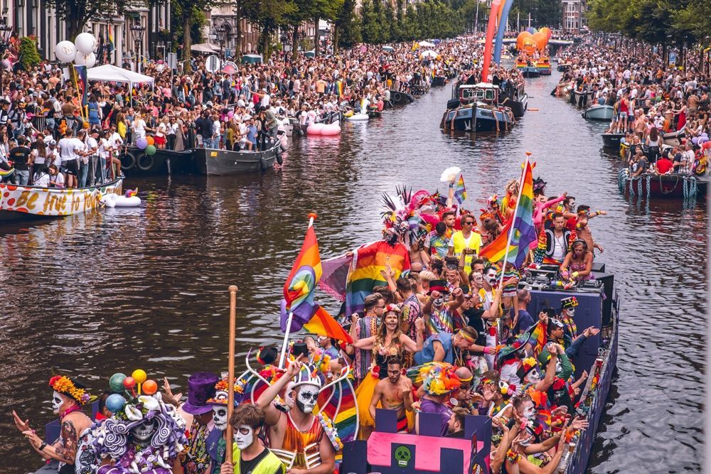 Amsterdam Pride parade: Boats filled with people celebrate on a canal, rainbow flags waving amidst a large crowd lining the banks.