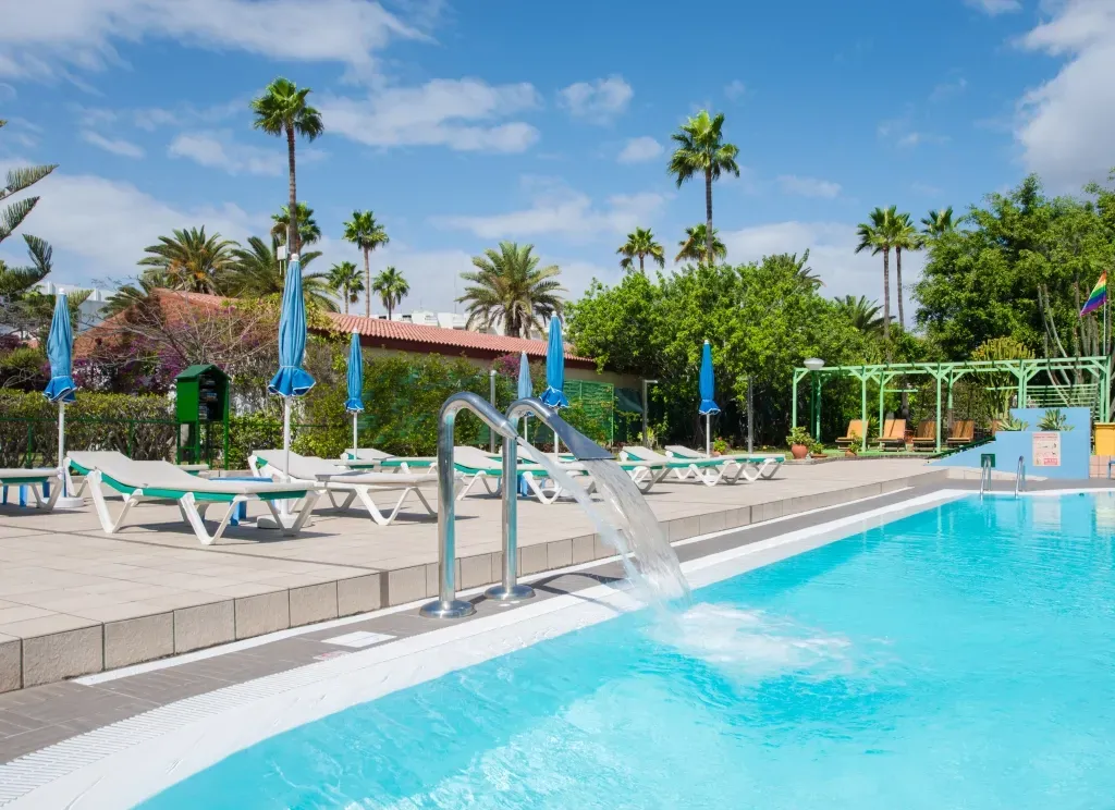 A large swimming pool surrounded by chairs and palm trees on a sunny day.