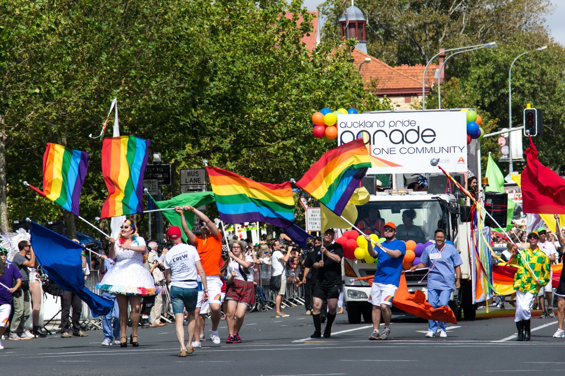 People march in a Pride parade, waving rainbow flags. A float with