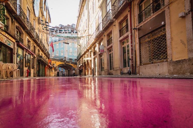 Pink-paved street in Lisbon with shops on either side and an archway at the end.
