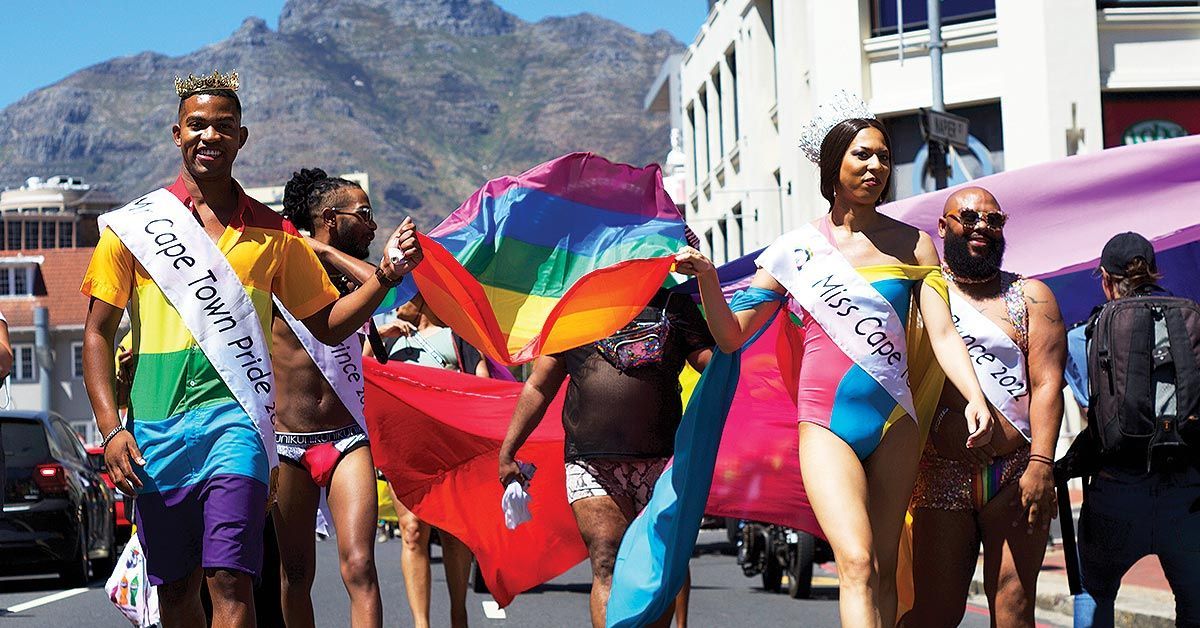 People marching in a Pride parade, carrying a rainbow flag. Sunny day, city street. Cape TOwn