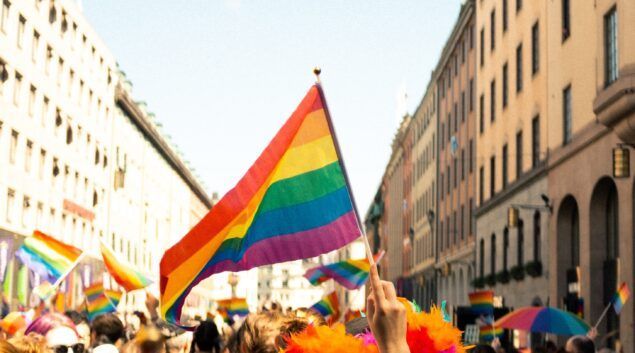 A vibrant rainbow flag waves at a Pride parade, held on a city street lined with buildings.Copenhagen Pride Festival (Denmark)
