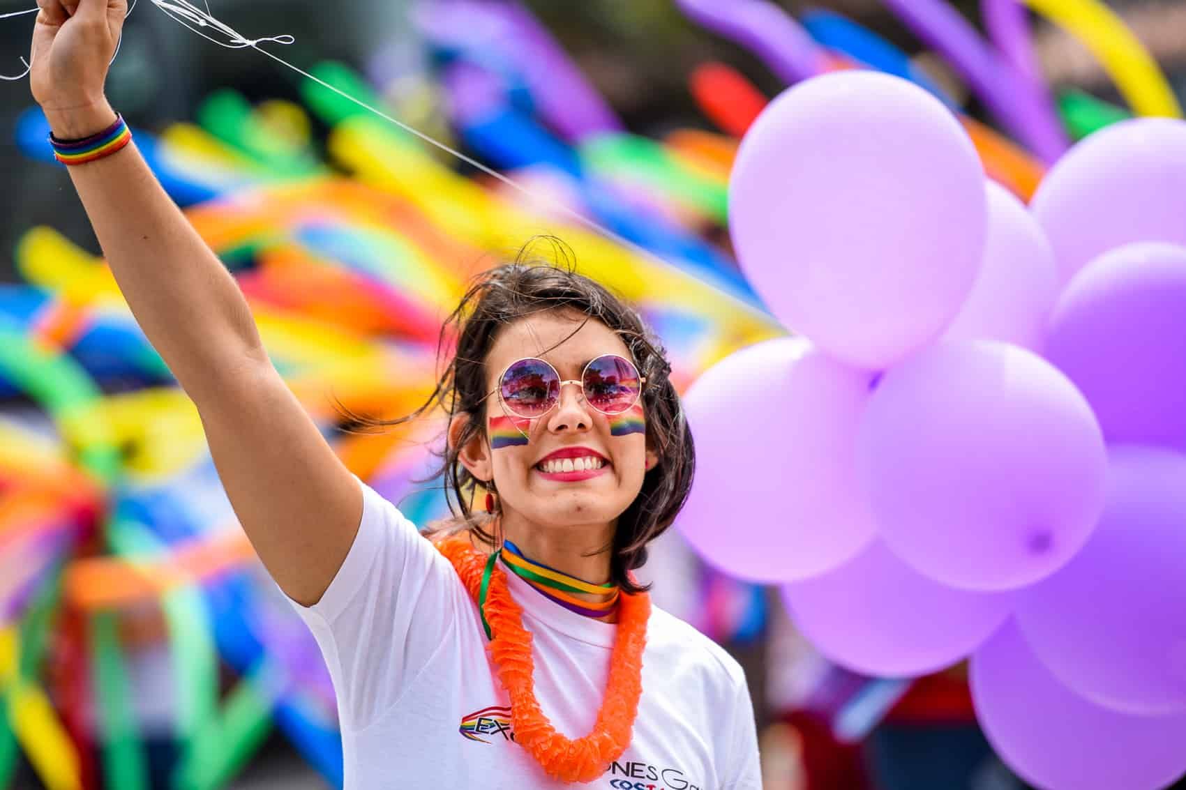 Smiling person waving with raised arm amid colorful balloons at a festive parade