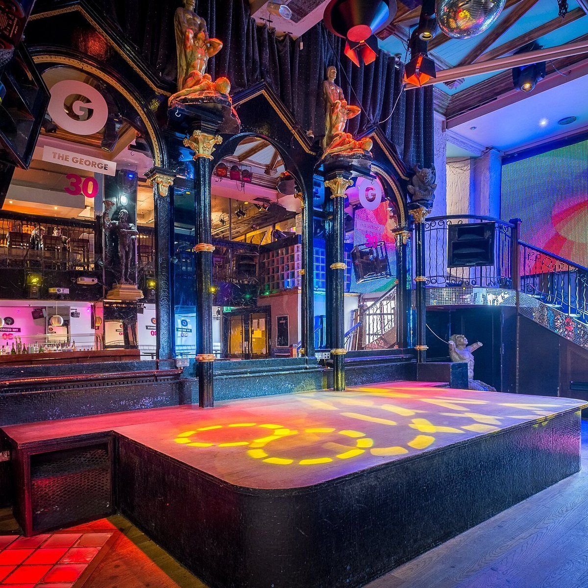A brightly lit, empty stage with dark, ornate pillars and glowing gold patterns on the floor in a theatrical venue.