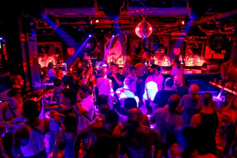 People dancing in a dimly lit nightclub with red and blue lights; disco ball.