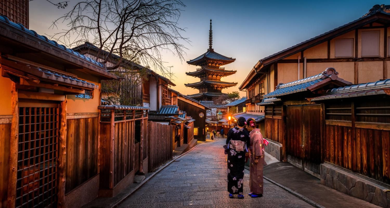 Narrow street in Kyoto, Japan, with traditional buildings and pagoda at the end, two women in kimonos.