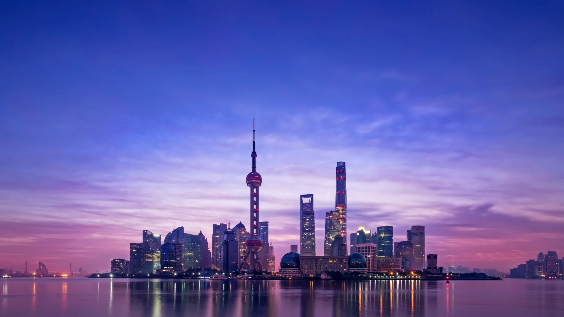 Shanghai skyline at dusk, buildings and TV Tower reflecting in water, purple and blue sky.