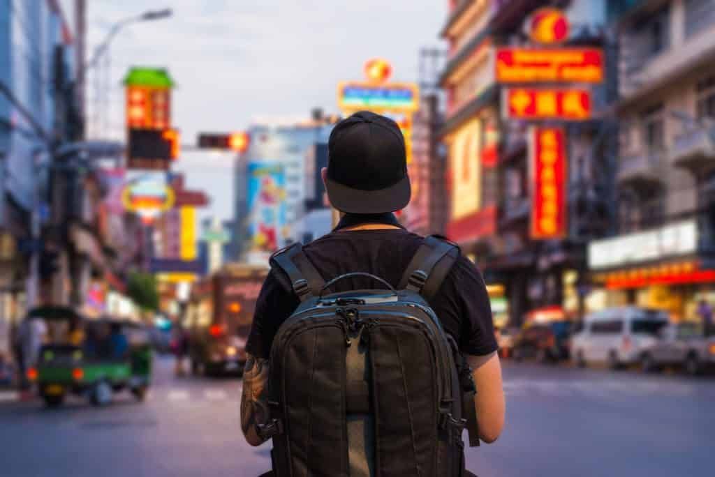Person with backpack walking down a street lined with signs, possibly in Chinatown, with blurred background.