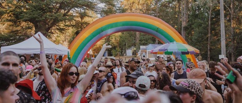 LGBT Music Festival A crowd celebrates under a large inflatable rainbow arch. People dance and raise their hands at an outdoor event.
