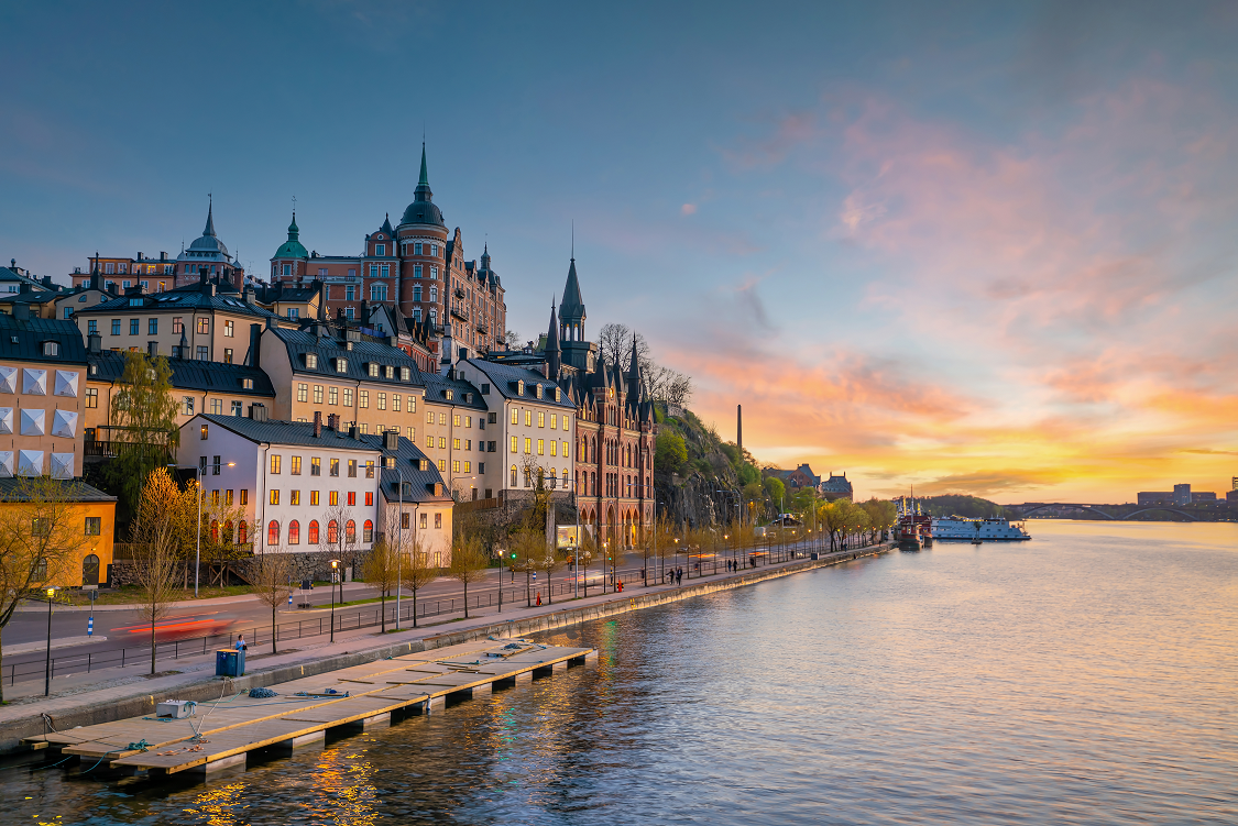Sunset over a waterfront city with historic buildings and a river reflecting pink-orange sky