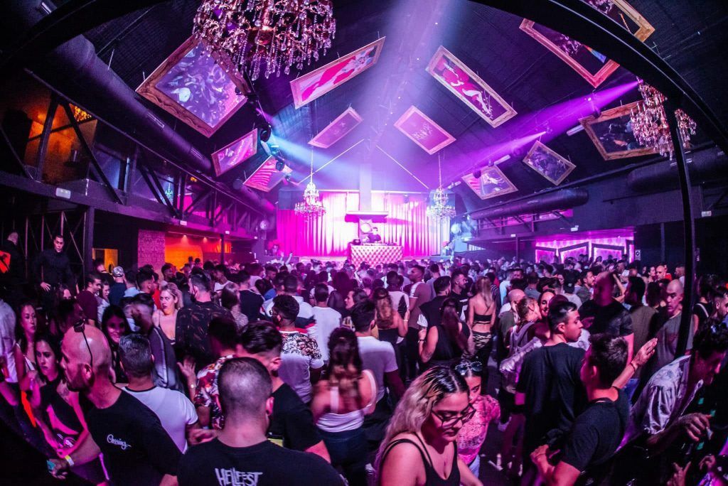 Nightclub with a crowd dancing; DJ on stage, pink and purple lighting.