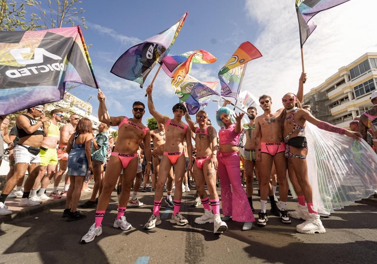 People in colorful outfits and waving rainbow flags at a Pride parade.