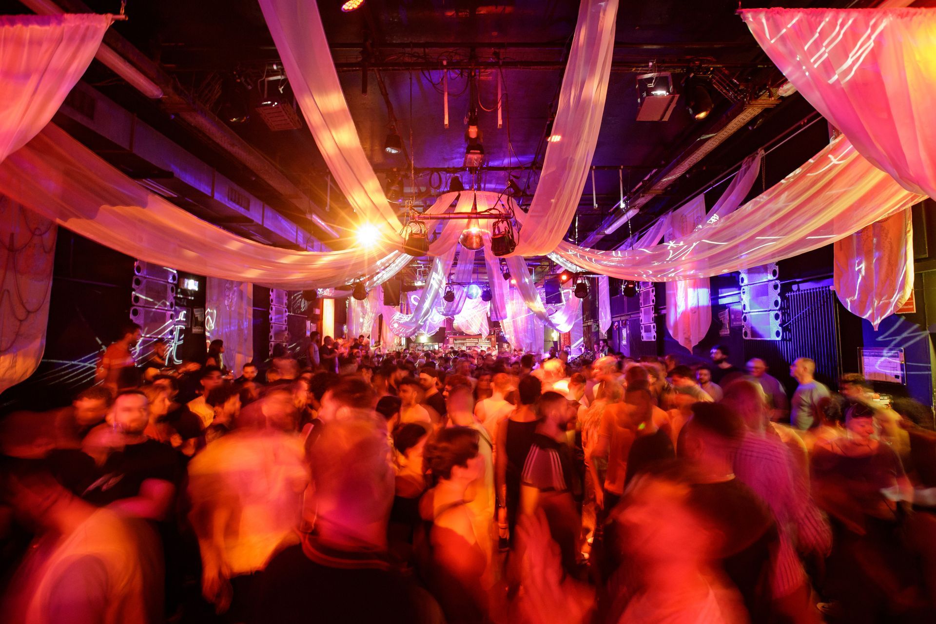 Party scene: People dancing in a crowded club with colorful lights, draped fabric, and a disco ball. Halloween Queer Fest (Berlin)