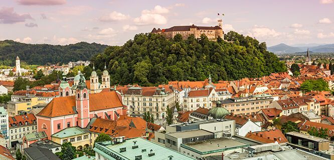 Aerial view of Ljubljana, Slovenia with a castle on a hilltop, and buildings with red roofs.