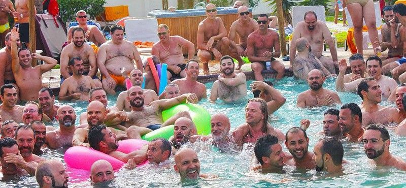 Men in a pool, some with floaties. Sunlight, smiles, and social gathering are evident. Maspalomas Bear Winter Sun (Gran Canaria)